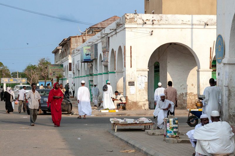 lady in red dress walks down a street in port sudan